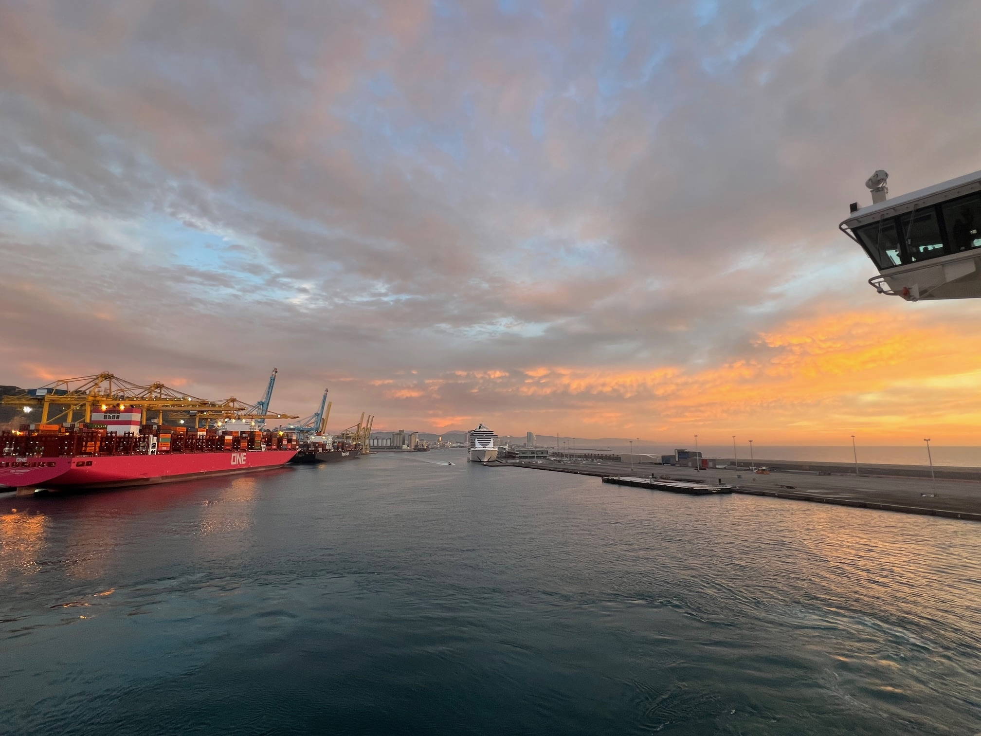 Kreuzfahrtschiff bei der Einfahrt in den Hafen von Barcelona - in der Ferne ein ONE-Containerschiff am Anleger
